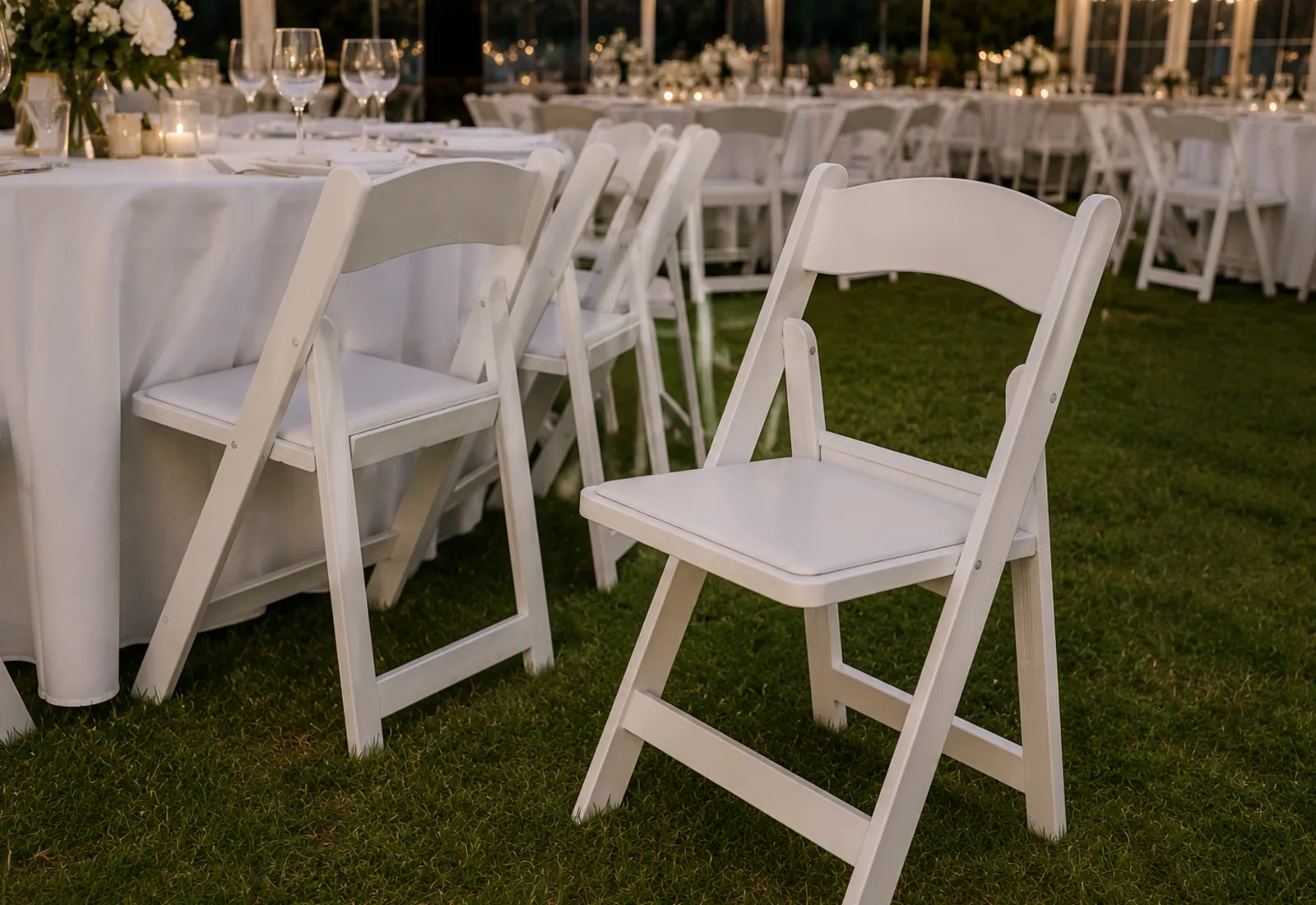 Rows of white folding chairs on a lawn for an outdoor ceremony
